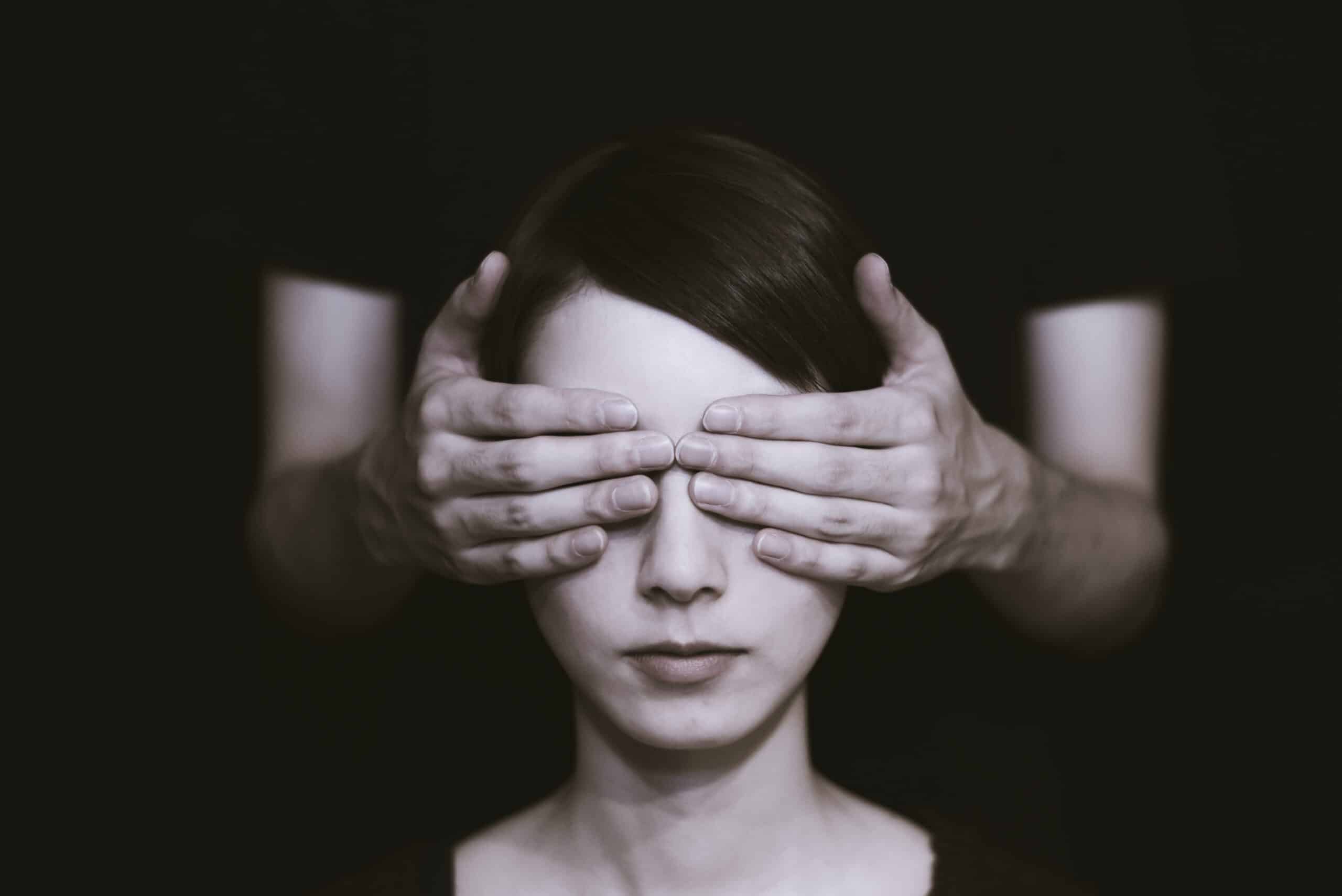 Woman sitting with person standin behind covering her eyes